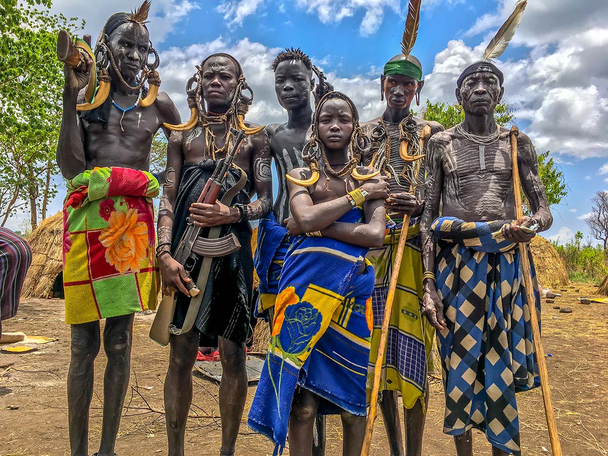 A group of Mursi people standing together in the Omo Valley, wearing beaded collars and brightly patterned cloth.